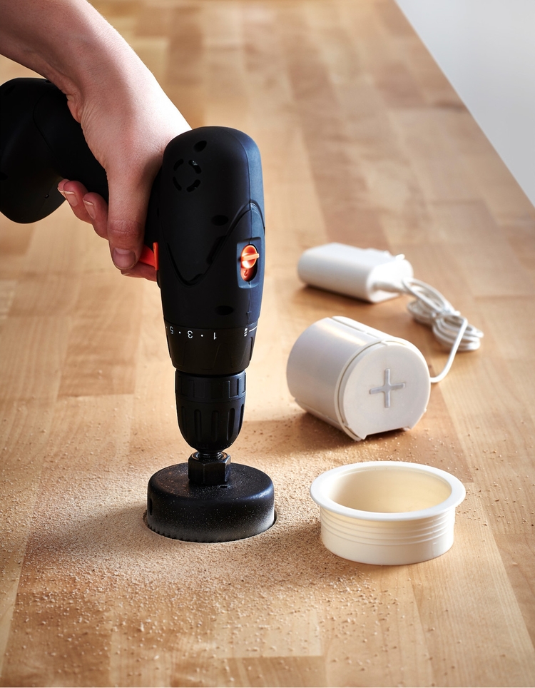 A person is installing IKEA's JYSSEN wireless charger into a wooden surface.