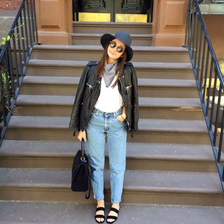 Alyssa Wasko is standing in front of a stoop and wearing a black hat, sunglasses, leather jacket, bag, shoes, and Donni Charm scarf