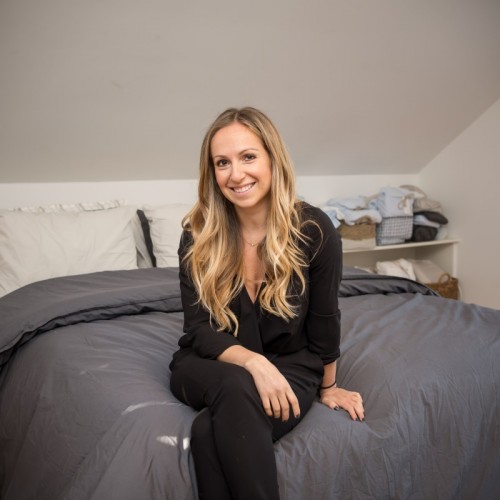 Parachute Founder and CEO Ariel Kaye, who is a MakeSpace NYC storage customer, is sitting on a made bed.