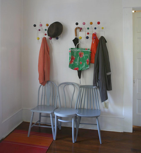Two Eames Hang-It-Alls are mounted to an entryway wall and storing two jackets, a hat, an umbrella, a bag, and a kids coat.