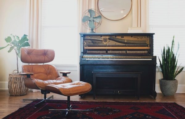 clean living room with eames chair, old piano, old fan carpet, houseplants, and a wall mirror