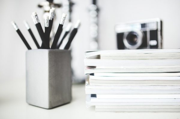 a desk with a pencil holder storing pencils, a stack of magazines, and a camera on top