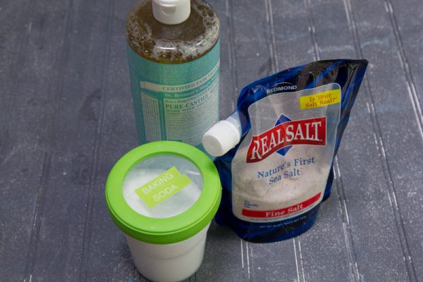 a plastic container of baking soda, a bottle of pure castille soap, and a bag of real salt sea salt for cleaning