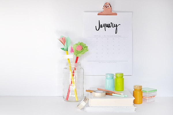 a hand-lettered calendar hanging above a desk with flowers on it