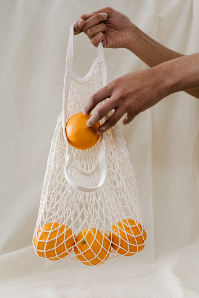 A hand placing oranges in a cloth bag