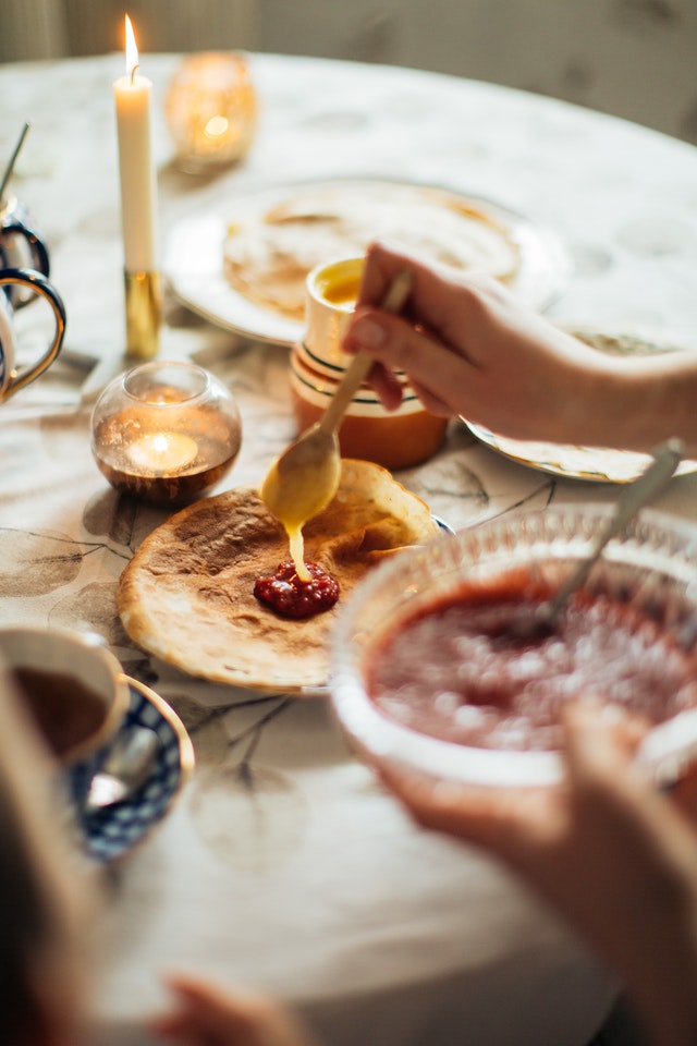 A food table with a hand serving themselves some hummus on a pita.