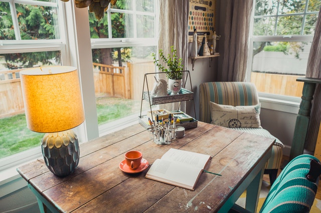 A table lamp and a cup on a table with a diary facing a window.
